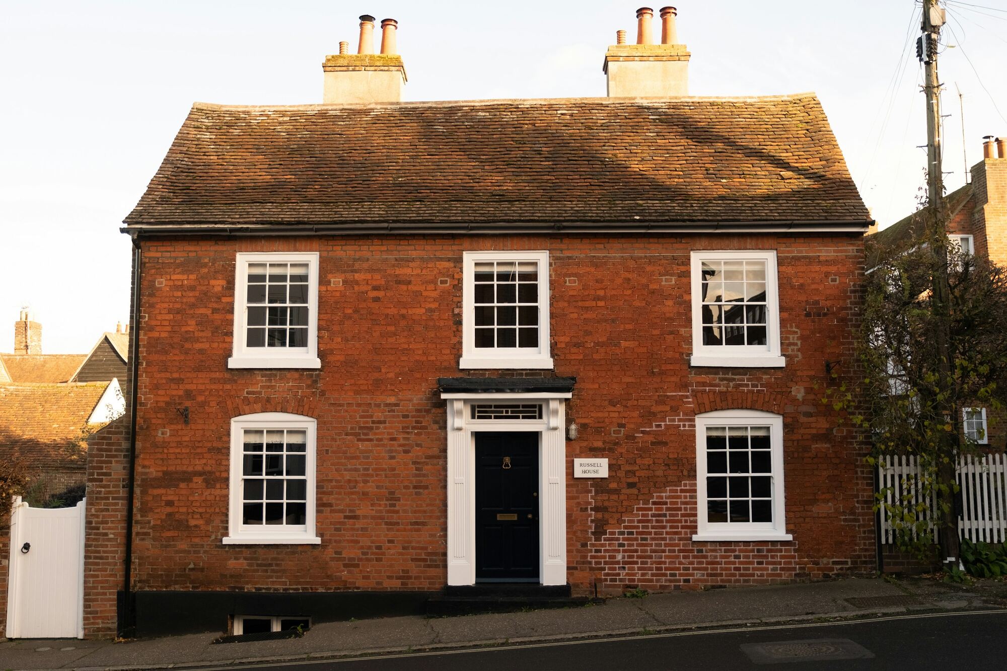 A red-brick house with white sash windows and a black front door, photographed from the street.